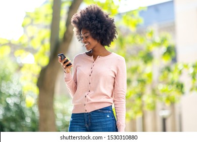 Portrait Of Smiling Beautiful Young Black Woman Looking At Mobile Phone Outside