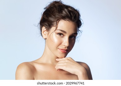 Portrait of smiling beautiful young girl with perfect glowing skin and bare shoulders on blue studio background. Beautiful natural woman looking at camera. Spa, skincare and wellness concept.