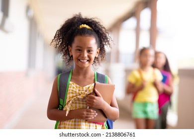 Portrait of smiling biracial elementary schoolgirl holding books while standing in corridor. unaltered, childhood, education and back to school concept. - Powered by Shutterstock