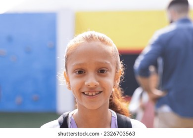 Portrait of smiling biracial elementary schoolgirl in school playground, copy space. Education, inclusivity, elementary school and learning concept. - Powered by Shutterstock