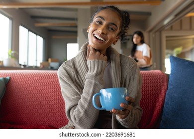 Portrait of smiling biracial mid adult woman with hand on chin and holding coffee cup on sofa. Copy space, unaltered, happy, drink, lifestyle and home concept. - Powered by Shutterstock