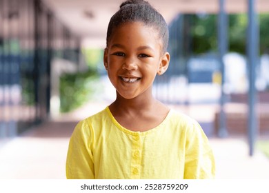 Portrait of smiling biracial schoolgirl standing in sunny school corridor with copy space. Education, childhood, inclusivity, elementary school and learning concept. - Powered by Shutterstock