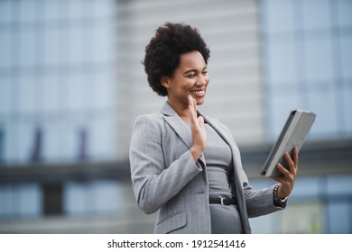 Portrait Of A Smiling Black Business Woman Making Video Call On A Digital Tablet In Front A Corporate Building.