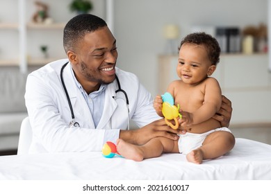 Portrait Of Smiling Black Doctor Making Medical Check Up For Little Baby Patient In Clinic, Handsome Young African American Pediatrist Looking At Adorable Infant Child In Diaper, Closeup Shot