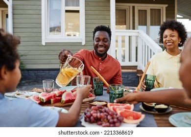 Portrait of smiling black man pouring orange juice to glass during family gathering outdoors - Powered by Shutterstock