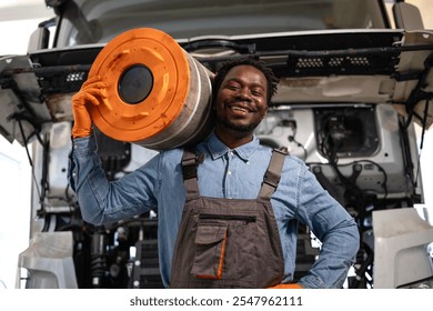 Portrait of smiling black mechanic in workshop standing by the truck and holding engine air filter. - Powered by Shutterstock