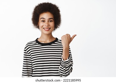 Portrait Of Smiling Black Millennial Woman Pointing Finger Right, Showing Advertisement, Company Logo Aside, Standing Over White Background