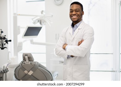 Portrait Of Smiling Black Stomatologist Doctor Wearing Uniform Posing In Modern Clinic Interior, Handsome African American Dentist Standing With Folded Arms And Smiling At Camera, Free Space