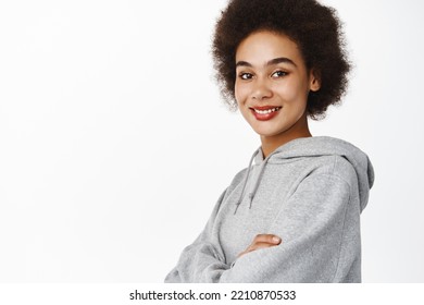 Portrait Of Smiling Black Woman With Afro Hair, Cross Arms On Chest, Wearing Grey Sporty Hoodie, Looking Happy And Confident, White Background