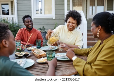 Portrait of smiling black woman pouring lemonade drinks to glass during family gathering outdoors - Powered by Shutterstock