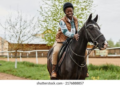 Portrait of smiling black woman riding horse in outdoor country ranch and stroking gently, copy space - Powered by Shutterstock