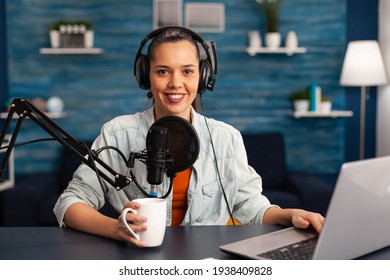 Portrait of smiling blogger looking at camera before starting live video at home studio podcast holding cup of coffee. Content creator blogger woman recording brodcast live streaming for Internet - Powered by Shutterstock