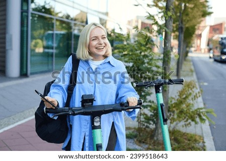 Portrait of smiling blond woman, college student using smartphone app to scan QR code on green electric scooter on street, renting a ride.