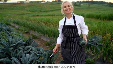 Portrait Of Smiling Blonde, Female Chef Picking Fresh Kale For A Farm To Table Restaurant.