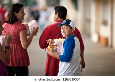 Portrait Of A Smiling Boy Carrying Snacks To A Baseball Game With His Family.