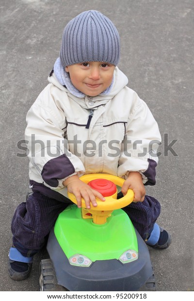Portrait of the\
smiling boy driving the toy\
car