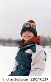 Portrait Of Smiling Boy In Knitted Hat On Winter Park Background. Winter Holidays. Vertical Frame