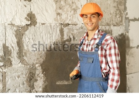 Portrait of smiling builder worker plasterer holding trowel to plastering cement wall in construction site. building construction work and industry concept