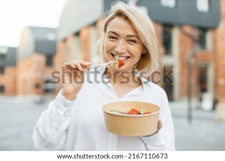 Portrait of smiling business woman eating healthy salad while having break during work. Kind positiv female eating her salad while being on the city street.