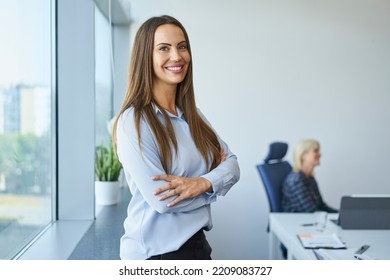 Portrait of smiling business woman standing at modern office with arms crossed looking at camera - Powered by Shutterstock