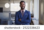 Portrait Of Smiling Businessman With Folded Arms Wearing Suit Working In Empty Open Plan Office