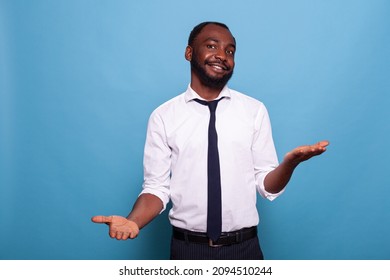 Portrait of smiling businessman with open palms weighing options on blue background. Confident office worker doing hand gesture comparing pros and cons putting decision in balance. - Shutterstock ID 2094510244