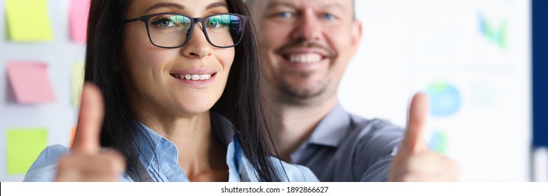 Portrait of smiling businesswoman and businessman looking at camera with gladness and calmness. Employees showing thumbs up. Company and business concept