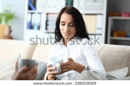 Portrait of smiling businesswoman having coffee break in office. Biz manager holding cup of tea and talking about work. Businesslady sitting on sofa and looking down with gladness. Business concept