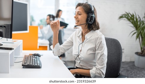 Portrait of smiling businesswoman listening to client via headset and answering customer calls in call center office. - Powered by Shutterstock