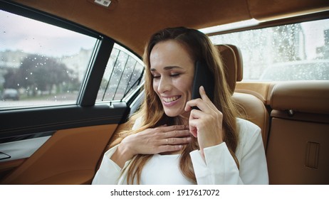 Portrait Of Smiling Businesswoman Speaking On Smartphone In Modern Car. Cheerful Business Woman Talking On Phone In Business Car. Elegant Lady Laughing In Back Seat Of Luxury Automobile.