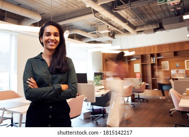 Portrait Of Smiling Businesswoman Standing In Busy Modern Open Plan Office