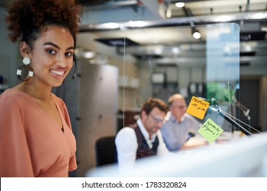 Portrait Of Smiling Businesswoman Standing By Glass Shield With Reminder Notes At Creative Office During Coronavirus