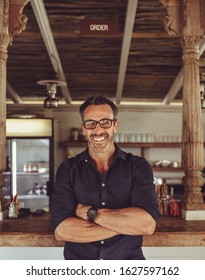 Portrait Of A Smiling Cafe Owner Standing With His Arms Crossed. Handsome Coffee Shop Owner Looking At Camera And Smiling.