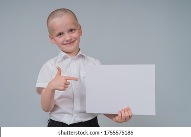 Portrait Of A Smiling Caucasian Boy 7 Years Old, Holding A Blank Sheet Of Paper