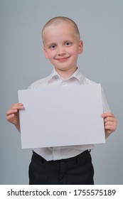 Portrait Of A Smiling Caucasian Boy 7 Years Old, Holding A Blank Sheet Of Paper