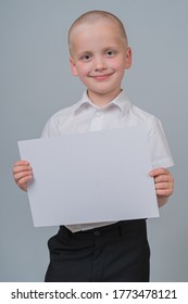 Portrait Of A Smiling Caucasian Boy 7 Years Old, Holding A Blank Sheet Of Paper