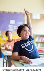 Portrait Of Smiling Caucasian Child With Raised Hand In Class. Primary Education. Back To School.