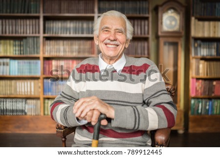 Portrait of a smiling caucasian elderly man sitting in a chair in the library