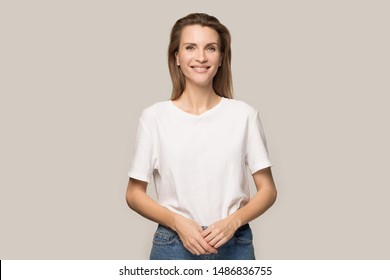 Portrait of smiling Caucasian millennial woman in casual clothes isolated on grey studio background, happy beautiful young female model wearing jeans and T-shirt look at camera posing for picture