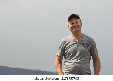 Portrait Of Smiling Caucasian Senior Man Cap In Gray T-shirt With Black Baseball. Isolated On The White Background. Happy Old Man Resting After Hiking On Top Of The Mountain. Active Seniors Concept.