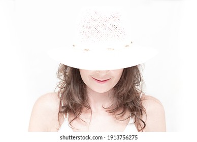 Portrait of smiling caucasian woman with long brunette hair. White summer hat and white tank top on white background. Overexposed summer photo. 