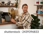 Portrait of smiling, charismatic young man, digital nomad working from cafe, sitting in coffee shop with laptop, turn head behind to look at someone, doing freelance project.