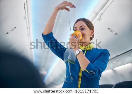 Portrait of smiling cheerful flight attendant demonstrating how grasping mask over nose and mouth while slip elastic band over head