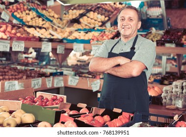 Portrait of smiling cheerful glad man seller who is standing in the vegetables store.