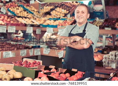 Portrait of smiling cheerful glad man seller who is standing in the vegetables store.