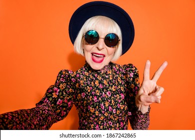 Portrait of smiling cheerful happy positive old woman take selfie showing v-sign isolated on orange color background - Powered by Shutterstock