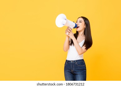 Portrait of smiling cheerful young pretty Asian woman holding megaphone making announcement in isolated studio yellow background - Powered by Shutterstock