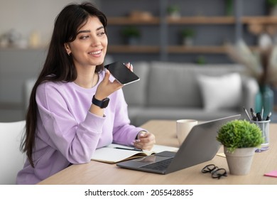 Portrait Of Smiling Cheerful Young Woman Sitting At Desk Using Laptop, Talking On Speakerphone, Dictating Voice Message, Using Online Translator App Or Voice Recognition Software, Virtual Assistant