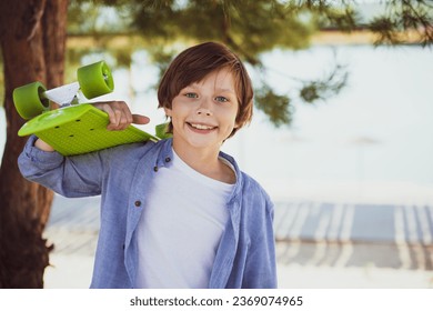 Portrait of a smiling child boy skateboarder holding a skateboard. Teenager with skating board at skate park looking at camera outdoors - Powered by Shutterstock