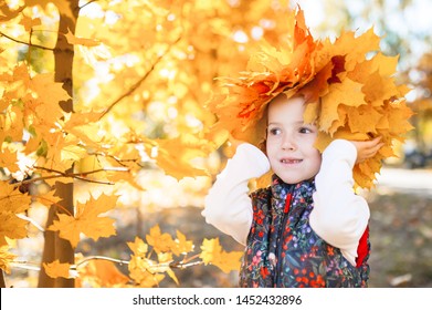 Portrait of smiling child with wreath of leaves on head. Background of sunny autumn park.